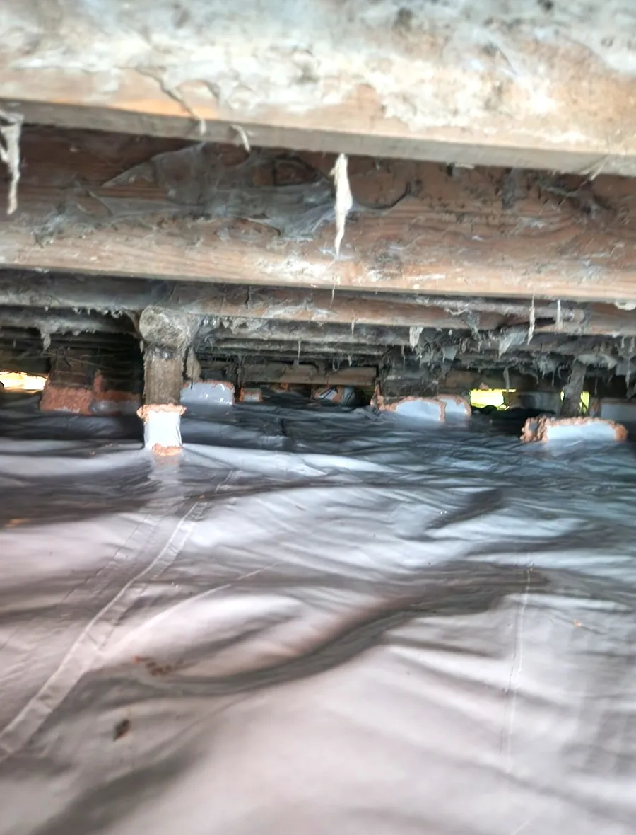 A completed white vapor barrier running the length of a crawlspace.